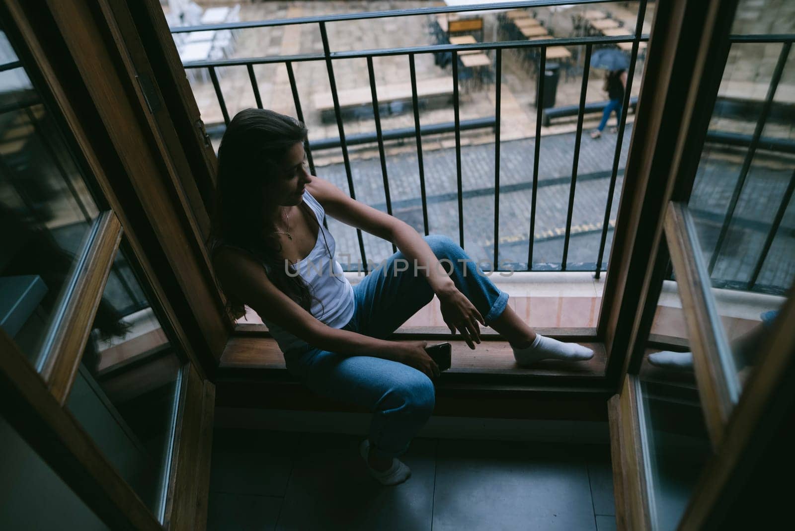 A young woman sits by the window, reflectively contemplating life in a stylish, tranquil urban setting
