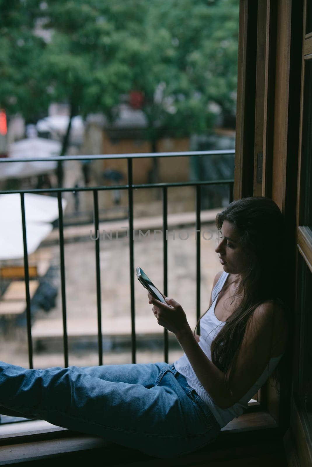 A peaceful and serene moment of a young woman deeply enjoying her phone while comfortably seated by the window