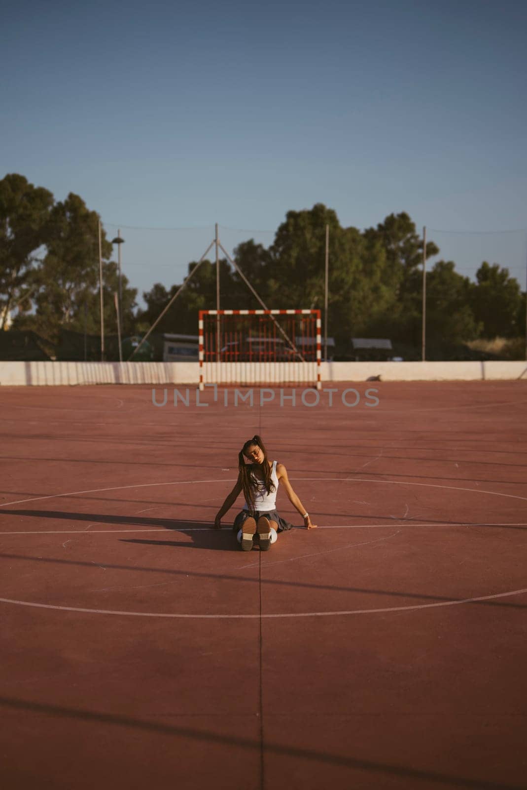 A tranquil scene of a young girl peacefully sitting alone on an empty basketball court during a beautiful sunset