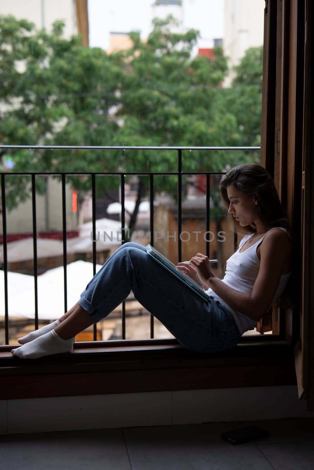 A woman finds enjoyment in a peaceful moment by her window, lost in deep thought and embraced by lush greenery