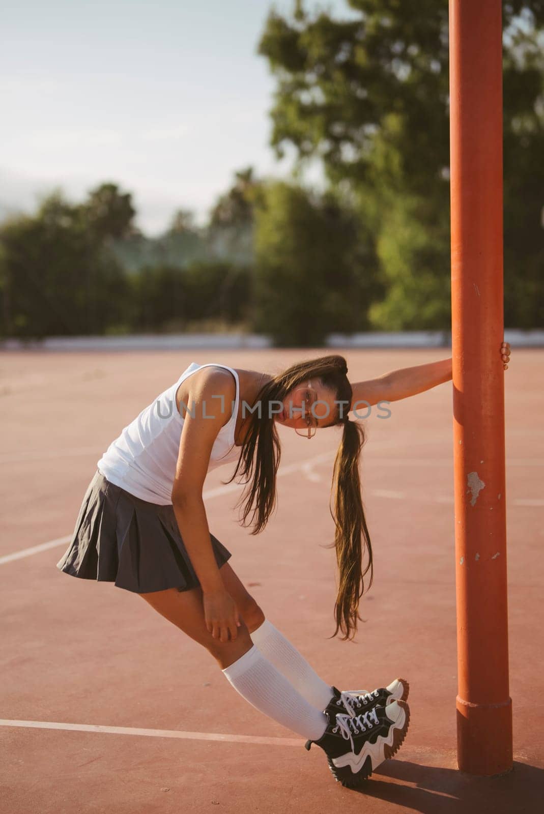 A young woman in sporty attire leans against a post on a sunny court, radiating confidence and positivity