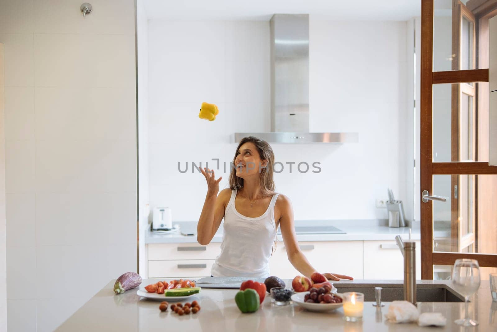 A playful woman skillfully juggling several pieces of cheese in a vibrant bright kitchen filled with fresh fruits