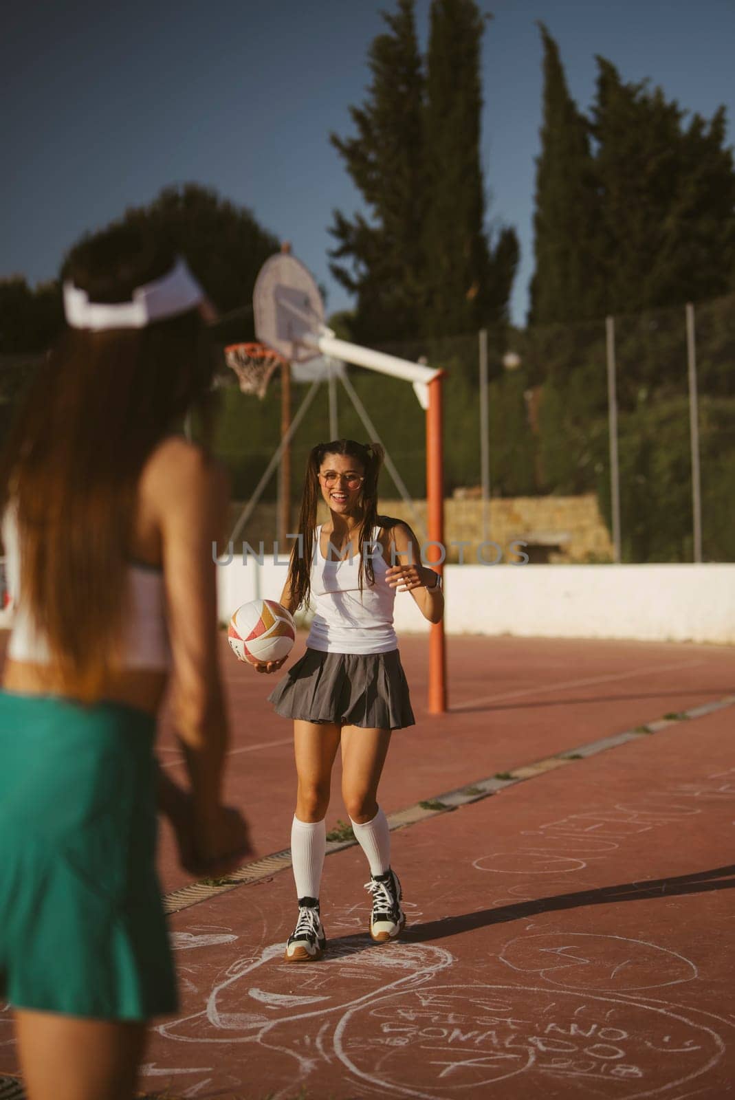 Two young girls are joyfully engaged in a lively and playful sports activity outdoors under the bright sun