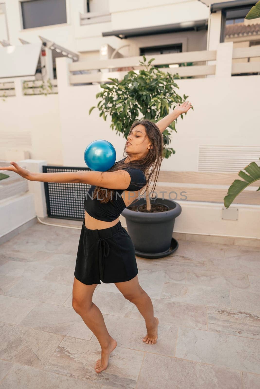 A skilled dancer performs an expressive move while balancing a bright blue ball in a lovely outdoor space