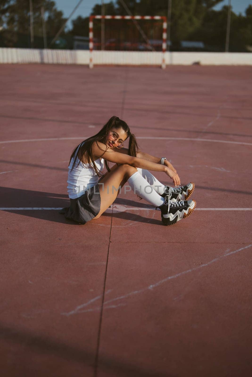 A stylish skater girl takes a refreshing break on a sunny court, showing her passion and relaxed vibe
