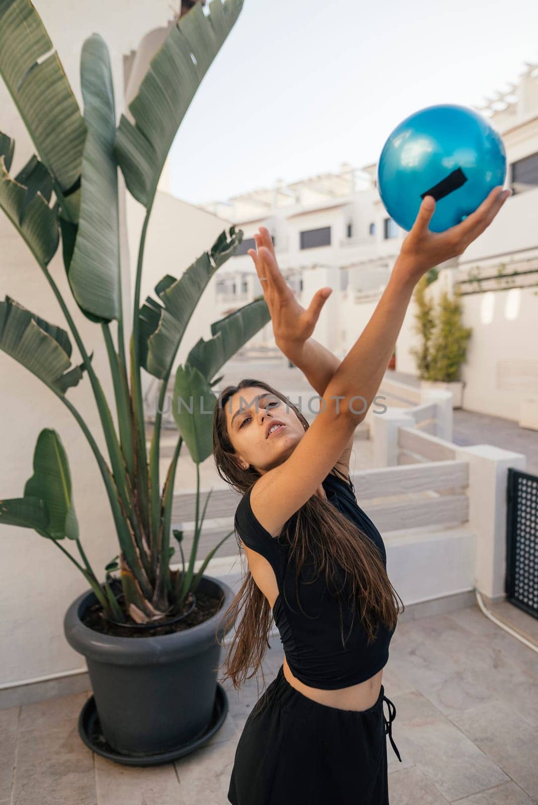 A woman poses elegantly and gracefully while holding a vibrant blue bowling ball, surrounded by lush greenery