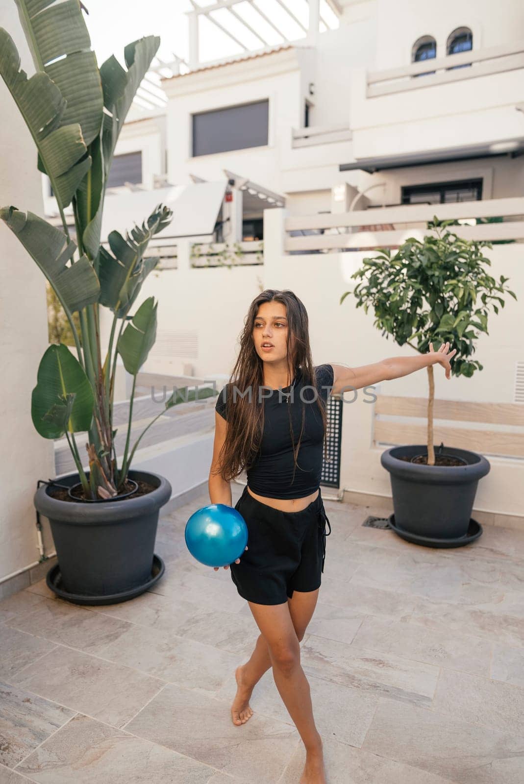 A young woman is casually playing with a vibrant blue ball in a stylish and modern outdoor environment