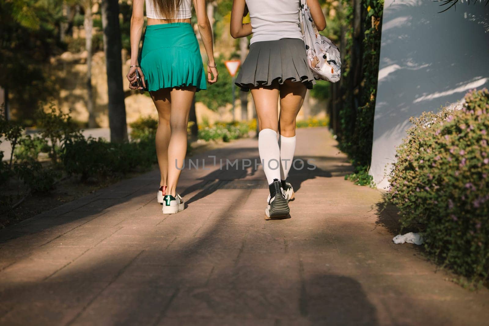Two young women happily stroll together in a sunlit park, showcasing their friendship and the leisure of life