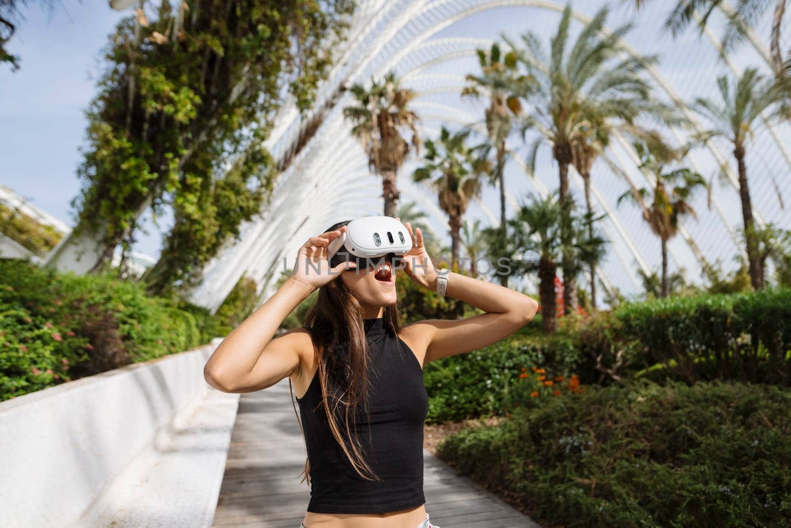 A young woman immersed in virtual reality, surrounded by vibrant greenery and sleek modern architecture