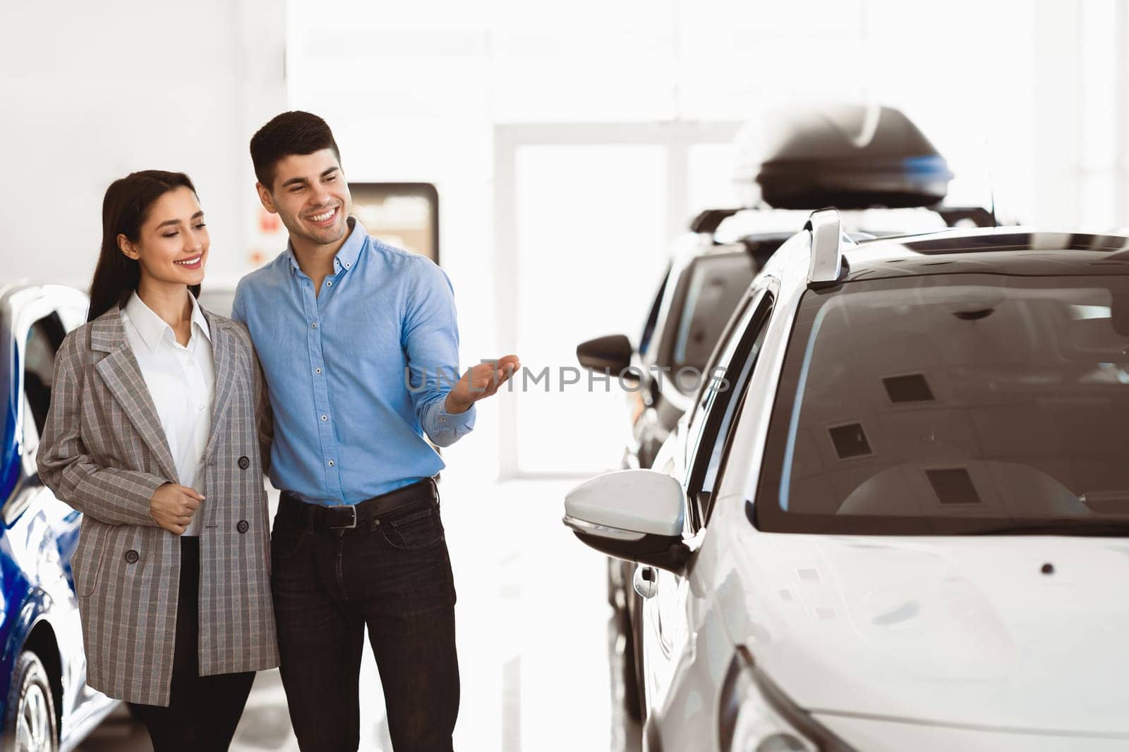 Visiting Car Dealership. Young family standing in auto showroom, looking for new vehicle