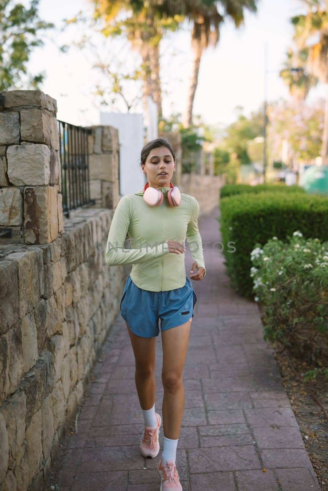 A woman jogs energetically along a beautiful path surrounded by palm trees and greenery in a serene setting