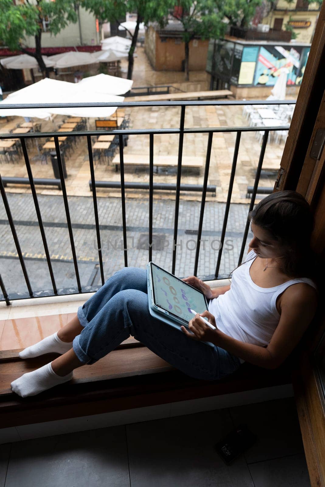 A woman is comfortably seated by the window, deeply engaged with her laptop in a calm and serene setting