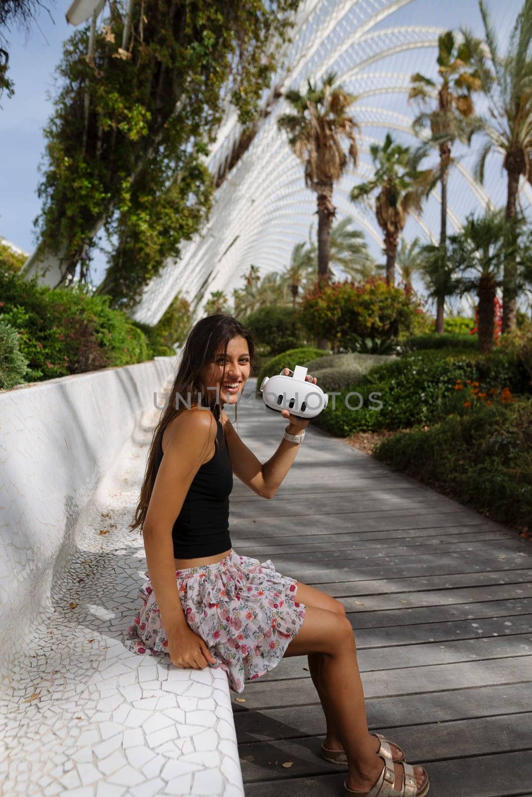 A woman sits in a beautiful park, enjoying a refreshing drink amid lush greenery and palm trees on a lovely day