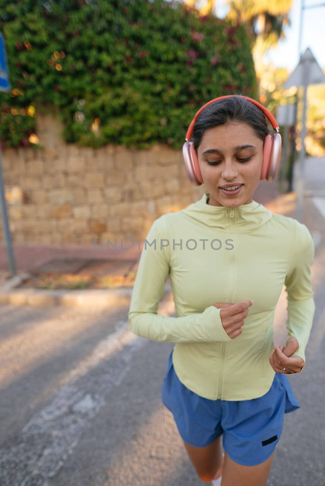 A young woman enjoys jogging outdoors in stylish sportswear and headphones, basking in the warm sun