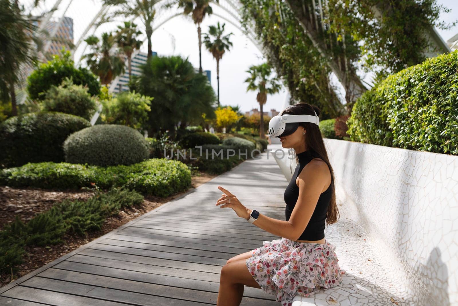 A woman experiences virtual reality while seated in a vibrant garden, blending nature and technology.