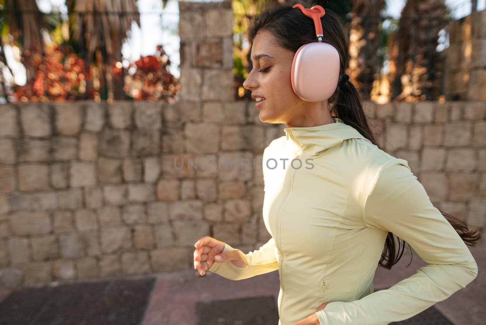 A woman jogs in a fashionable outfit while enjoying music through cozy ear muffs in an inviting outdoor setting