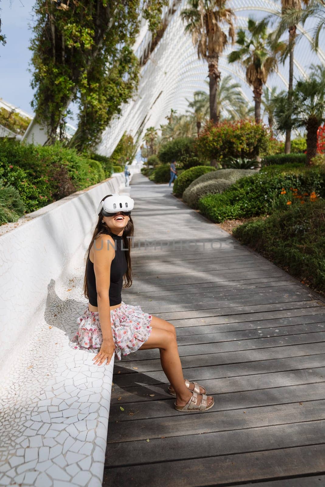 A stylish woman sits comfortably in a vibrant urban park, surrounded by greenery and modern design elements