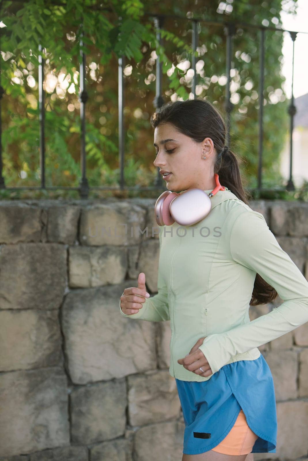 A determined girl jogs by a beautiful scenic stone wall, fully enjoying her invigorating workout with headphones on