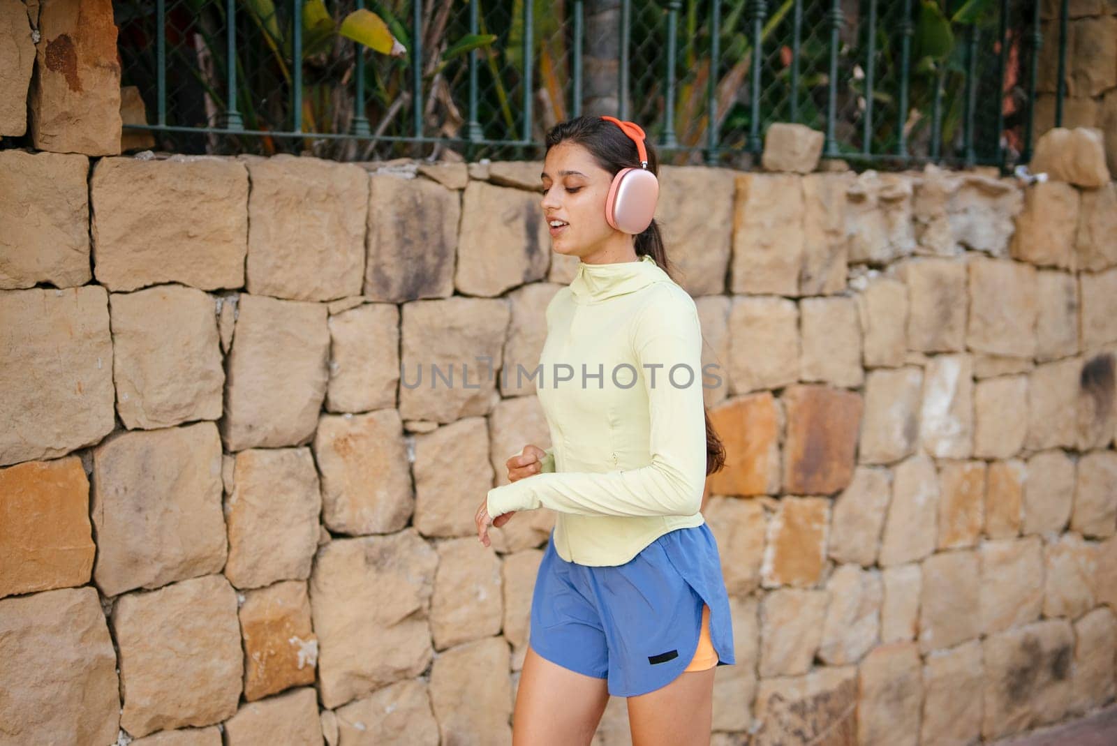 A young woman jogs outside, wearing headphones and comfortable clothing, showcasing an active lifestyle.