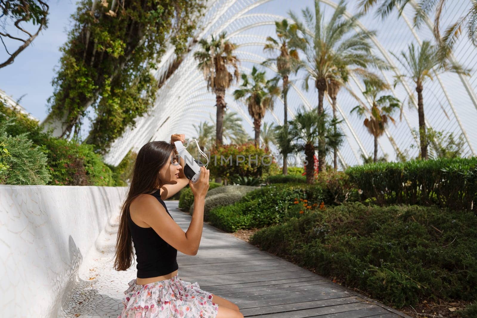 A young woman captures memories in a lush garden filled with palm trees and vibrant greenery around her