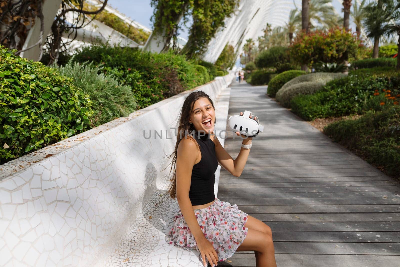 A cheerful young woman is happily seated outdoors, enjoying a tasty snack in a charming, vibrant green setting