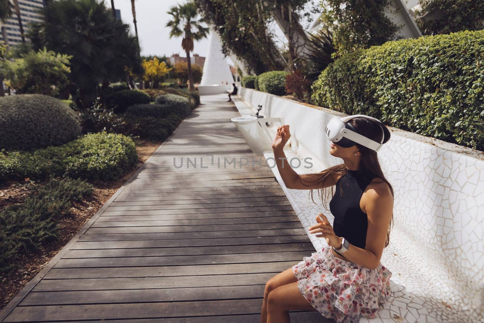 A young woman uses a VR headset, engaging with advanced technology in a vibrant, green outdoor setting