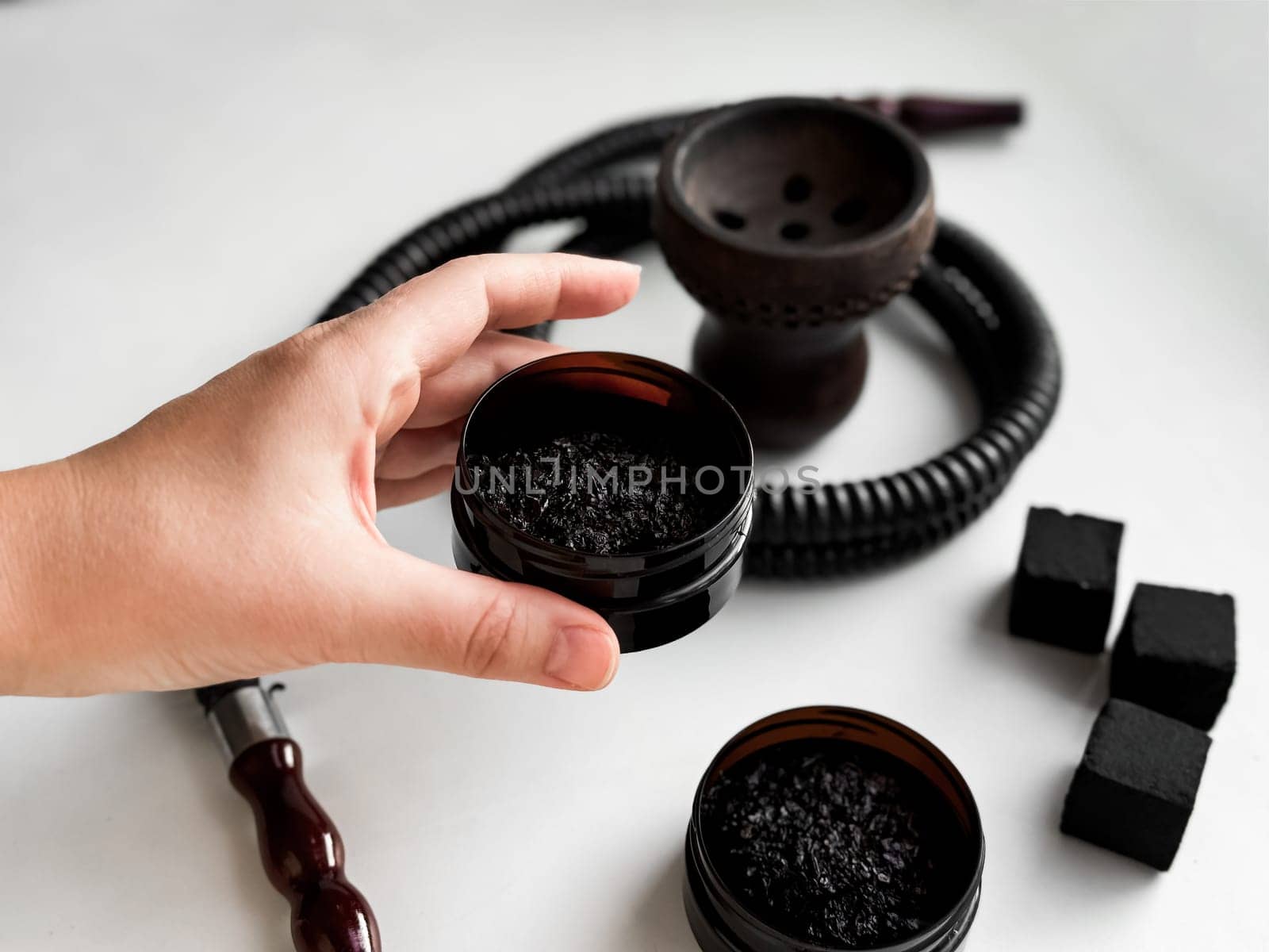 Hand holding hookah tobacco with shisha accessories and charcoal on white background.