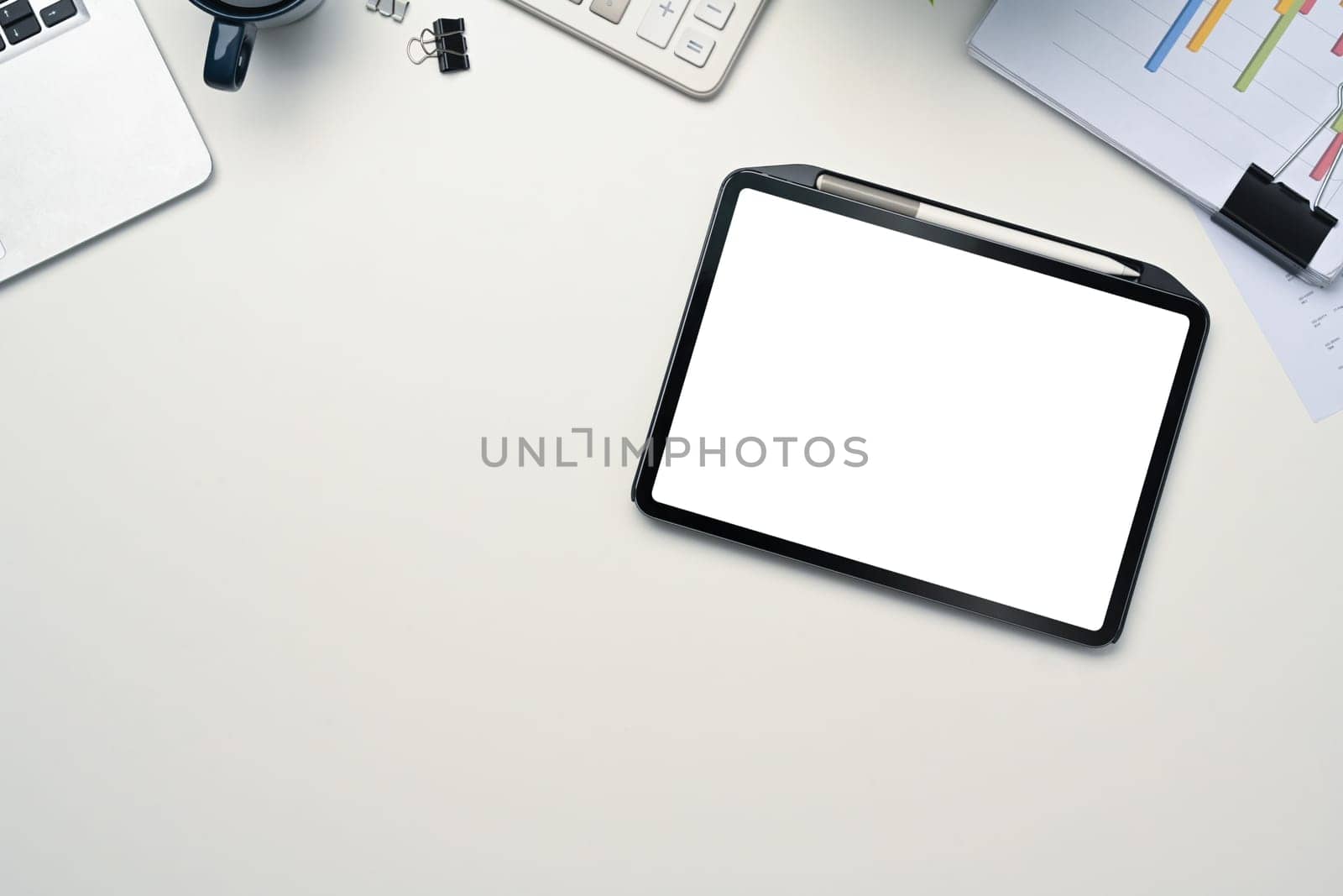 Digital tablet with empty display, laptop and financial document on white table.