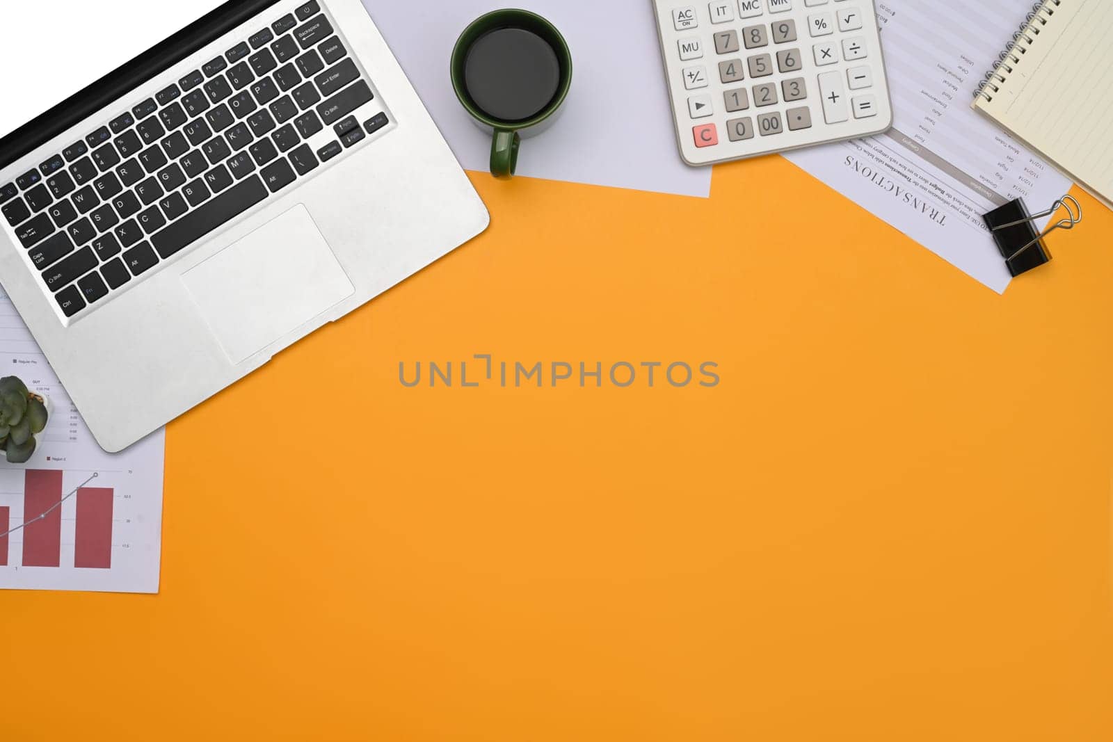 Top view laptop, financial reports, calculator and notepad on yellow background.