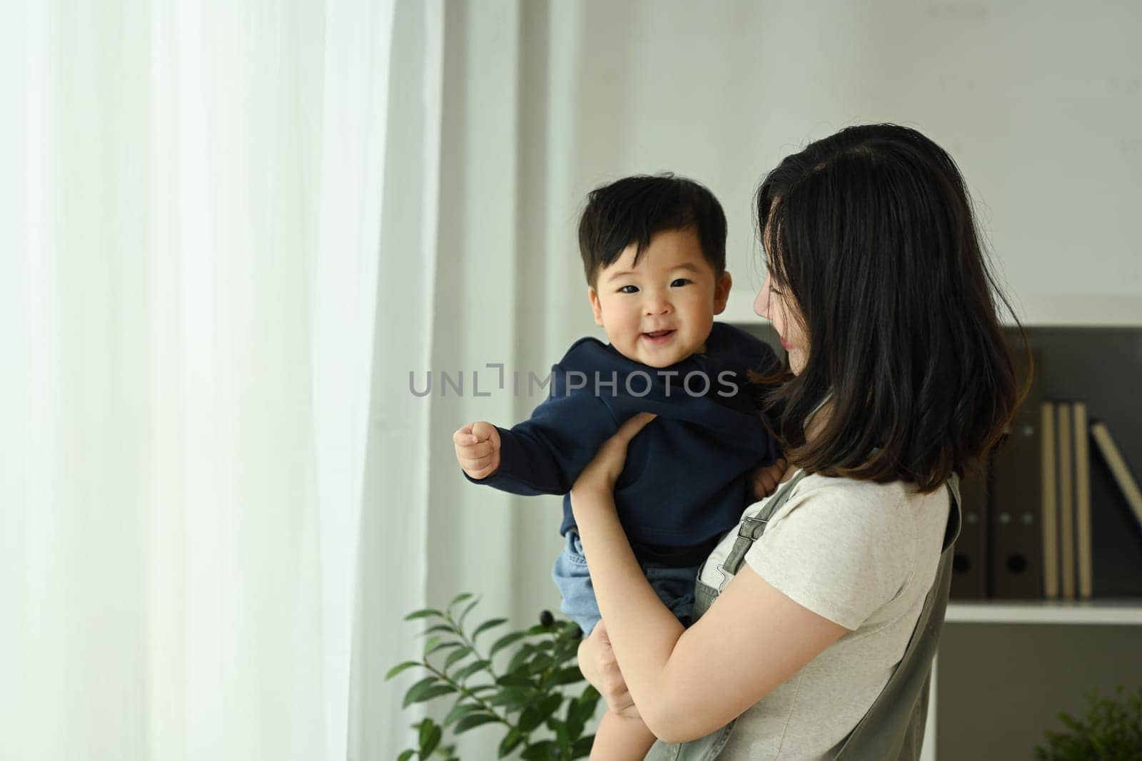 Loving asian mother holding her smiling baby in her arms. Family, love and childcare concept.