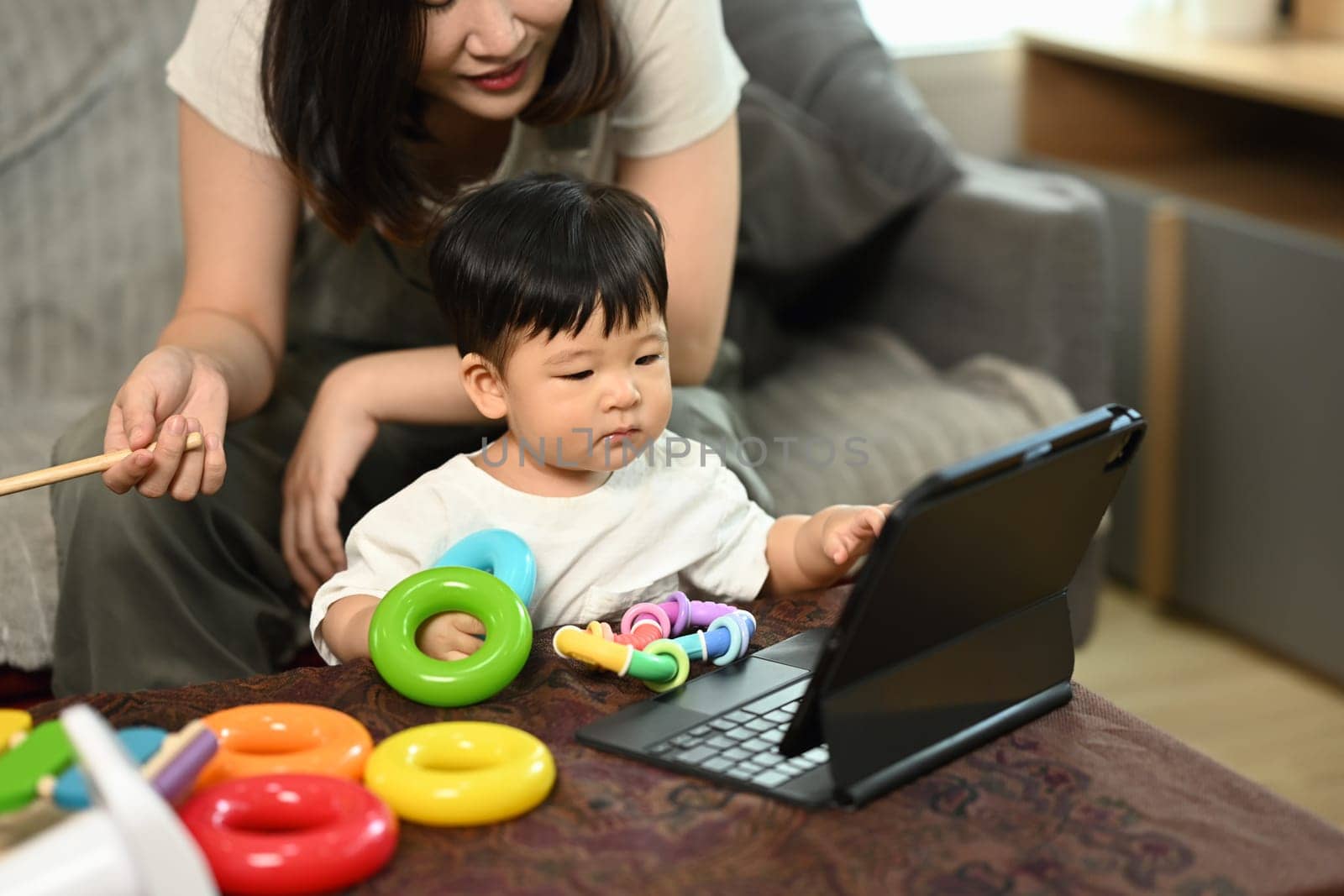 Cute little boy with mom sitting in living room looking at digital tablet screen.