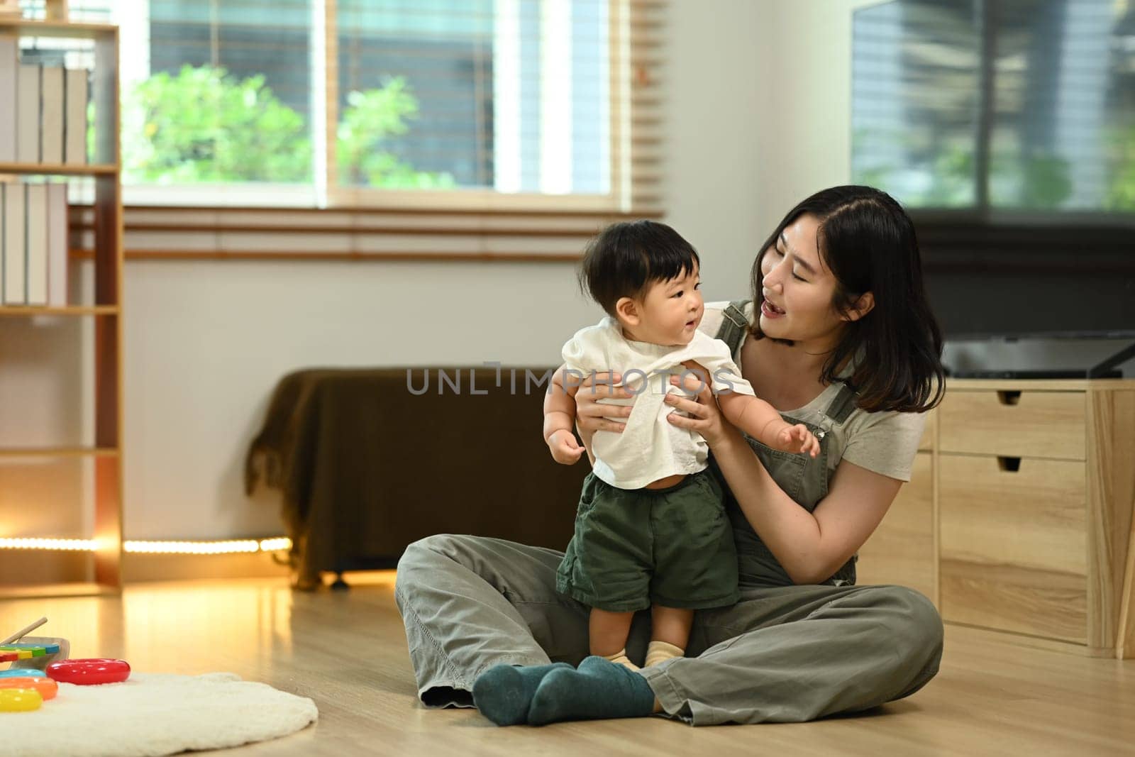 Happy young mother and her baby boy, playing together on the floor in cozy living room. Childcare concept.