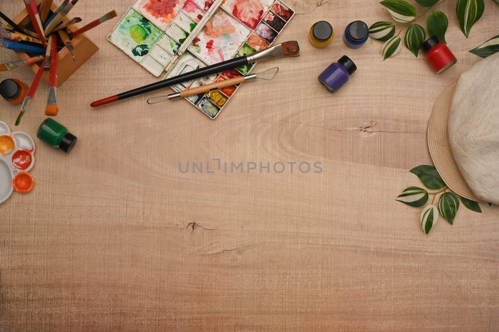 Variety of art supplies including paint brushes, watercolor paint and palette on wooden background.