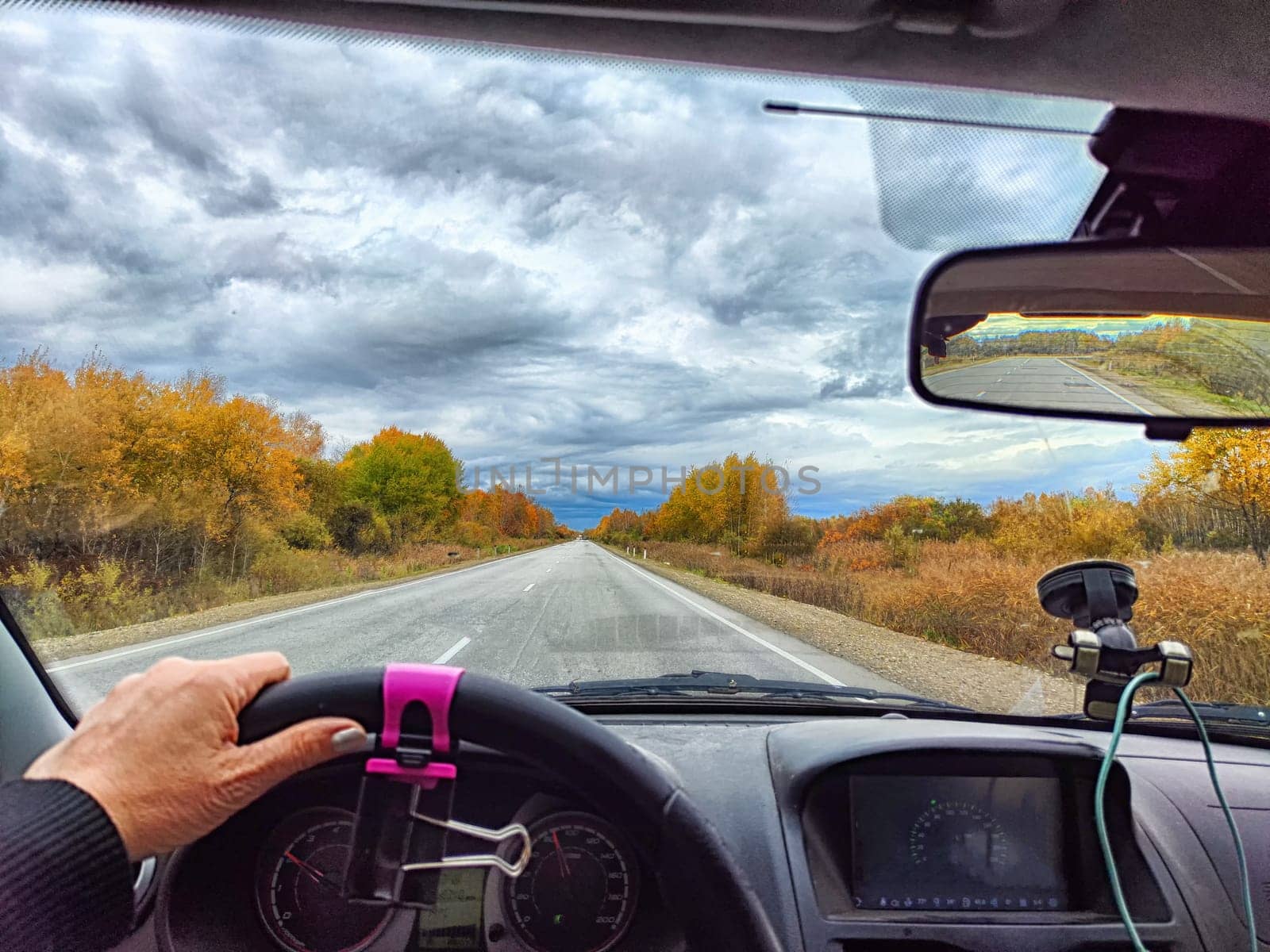 view through car windshield of nature landscape with green field, white clouds in blue sky. Hand of woman on steering wheel of car. Female traveler