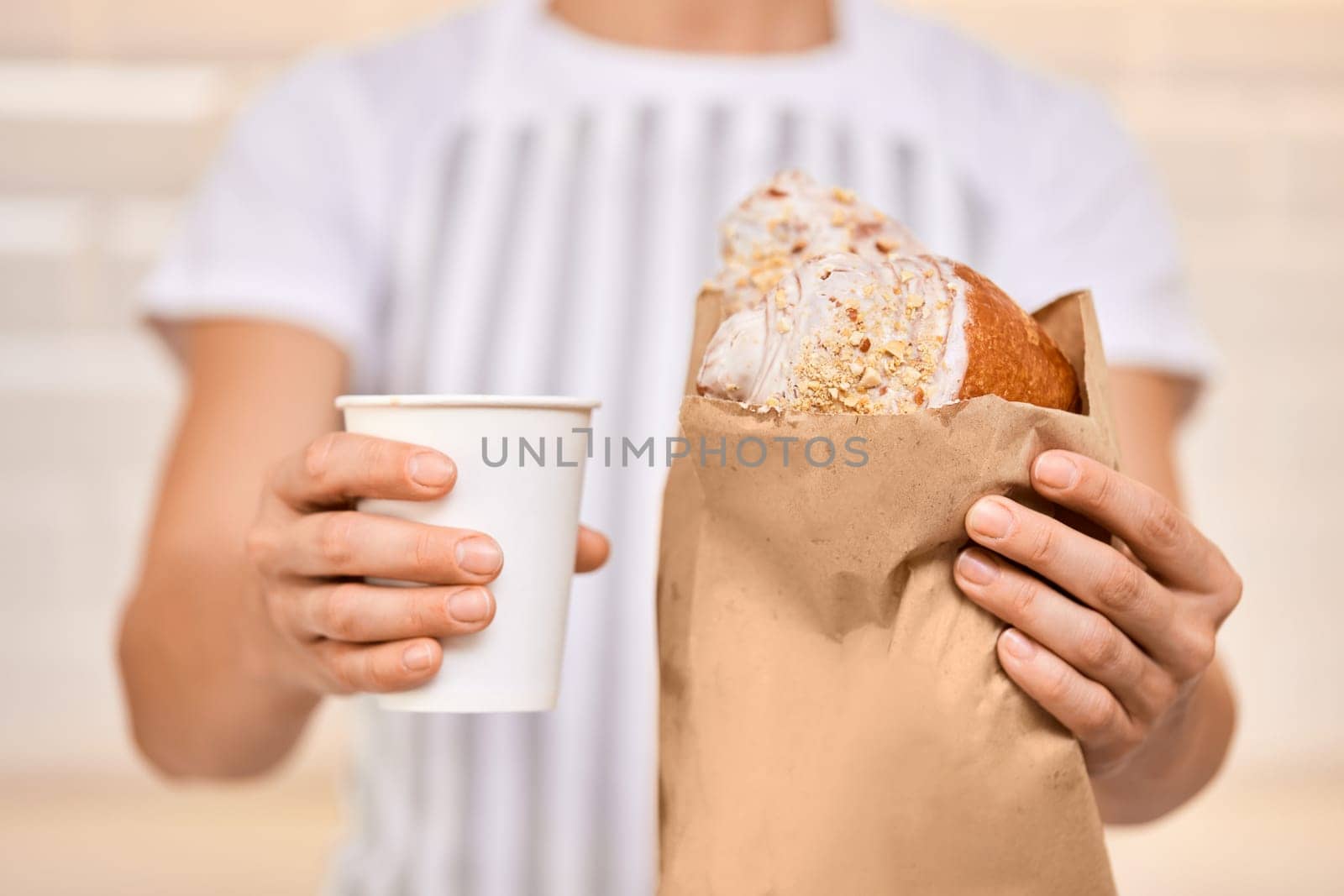 woman in apron is serving craft paper cup of coffee drinks and fresh croissant to customer