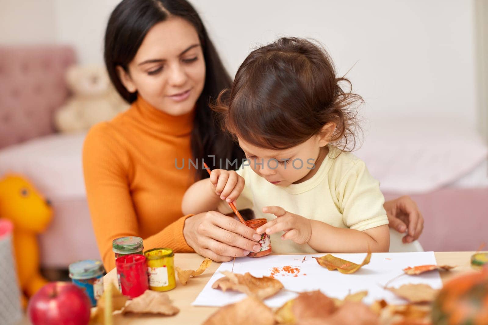 happy little child girl and her mother drawing for the autumn holiday. Happy family making autumn decorations together