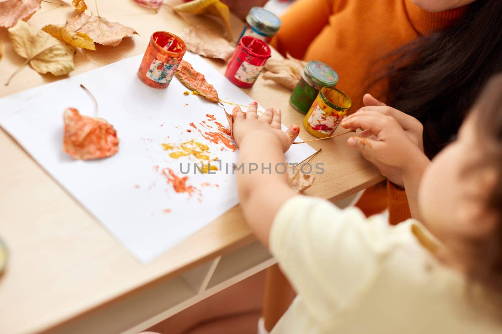 close-up, child and mom hands painting autumn yellow leaves together. happy time together at home
