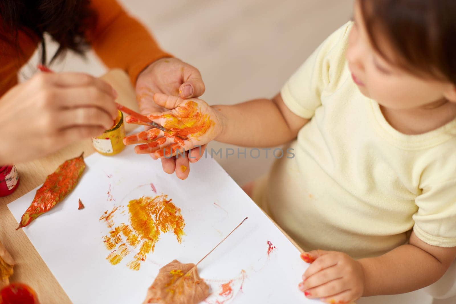 close-up, child and mom hands painting autumn yellow leaves together. happy time together at home