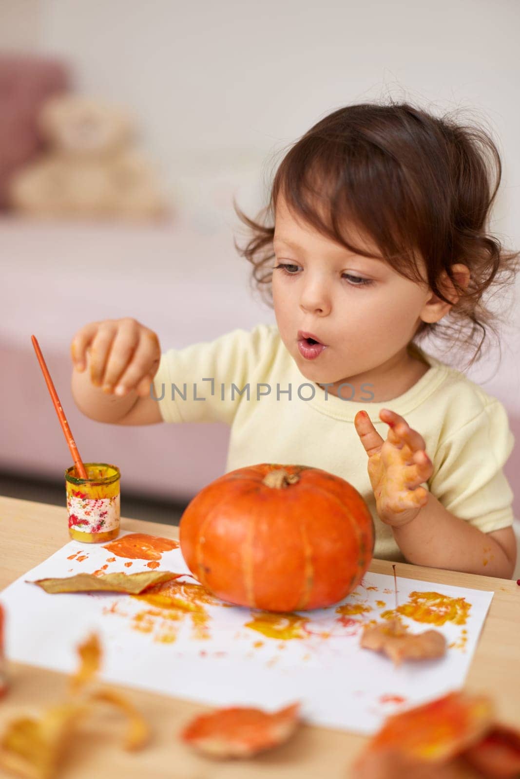 happy little child girl painting Halloween pumpkin. smiling baby girl drawing autumn pumpkin in yellow paint