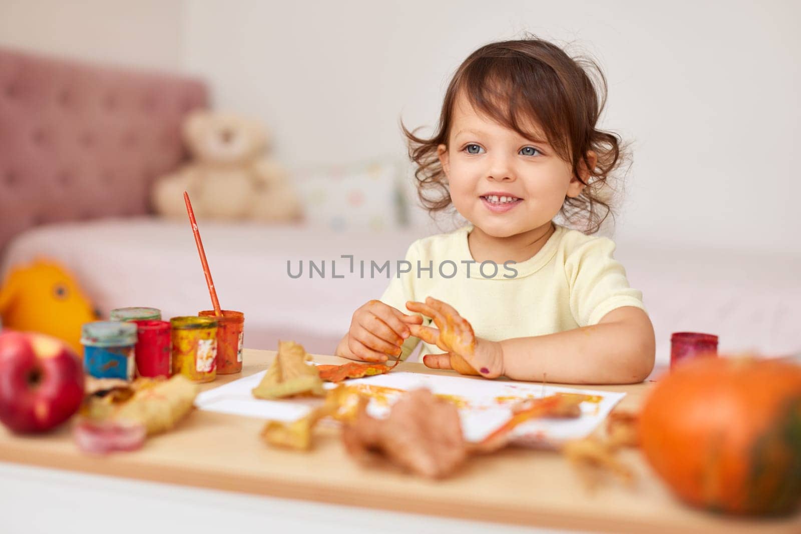 smiling little child girl painting autumn leaves. baby girl drawing leaves in yellow and orange paint