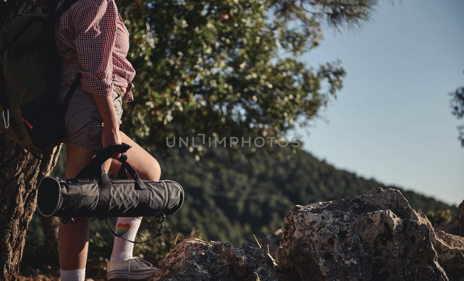 A hiker pauses on a rocky trail, carrying a yoga mat, surrounded by lush green forest. The scene captures the essence of outdoor adventure and mindfulness in nature.