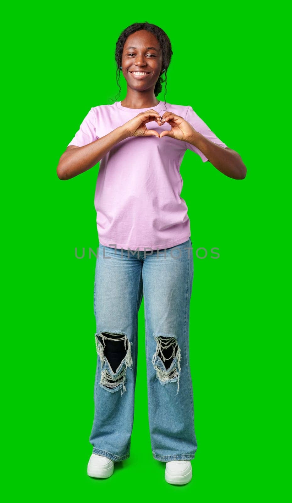 A young african woman expresses love by forming a heart shape with her hands against a bright green background