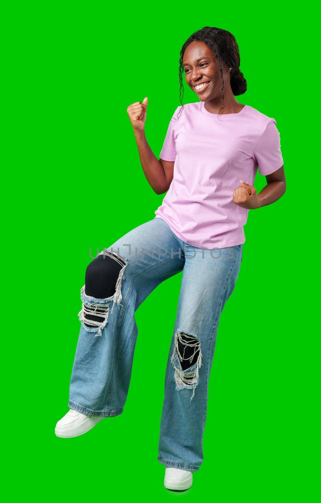 A young woman with braids expresses excitement with a clenched fist against a bright green background in studio