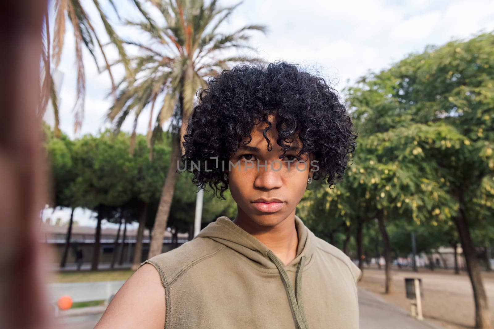 selfie photo looking at camera of a serious african american teenager with curly hair, concept of youth lifestyle and technology of communication