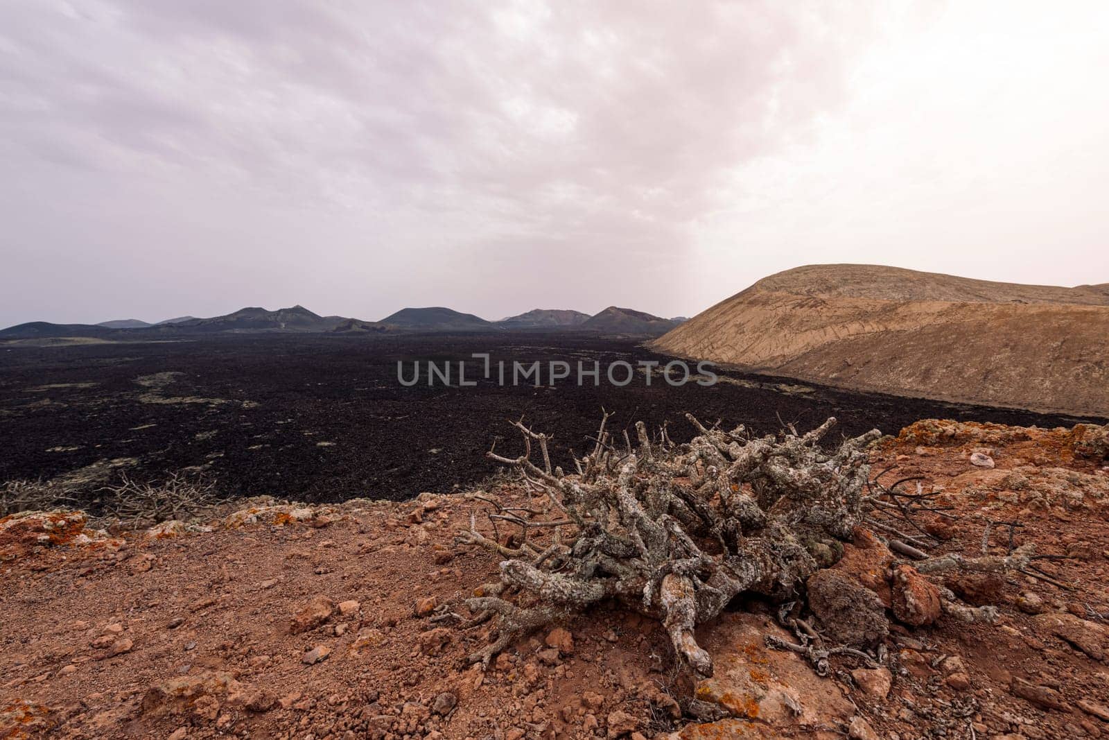 picturesque view of crater of volcano against mountains under light sky in Natural Park of Lanzarote in Canary Islands, Spain, concept of volcanic landscape and wild nature