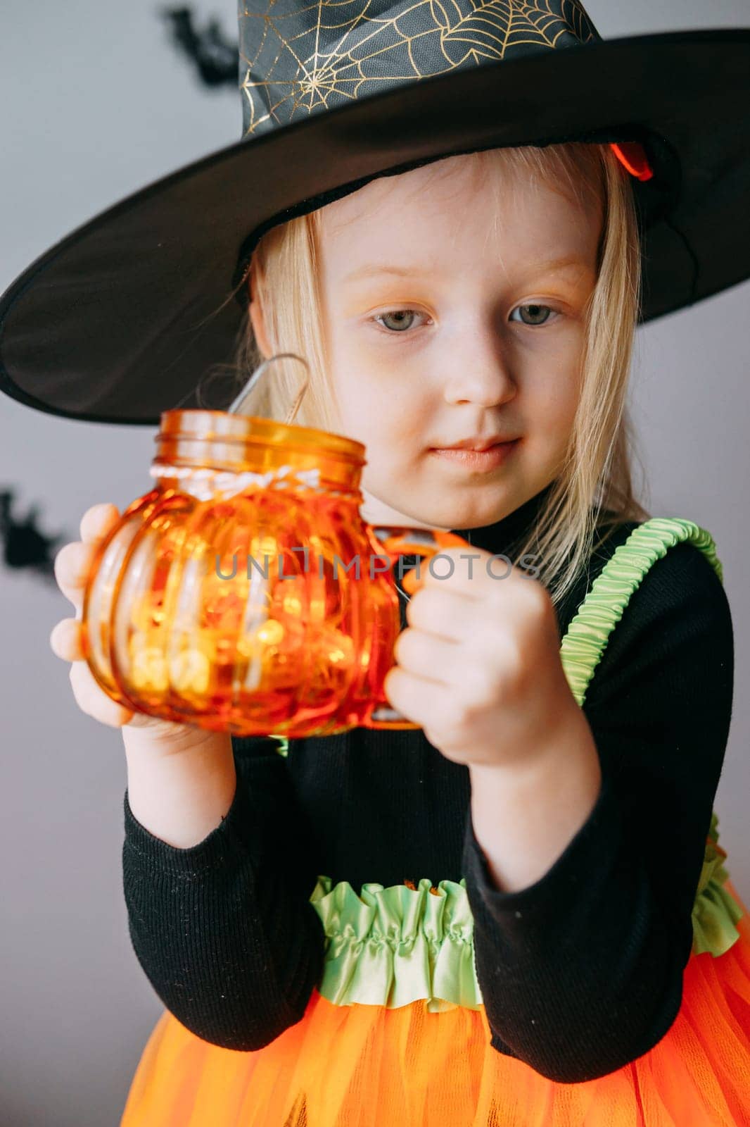 Children's Halloween - a girl in a witch hat and a carnival costume with airy orange and black balloons at home. Ready to celebrate Halloween.