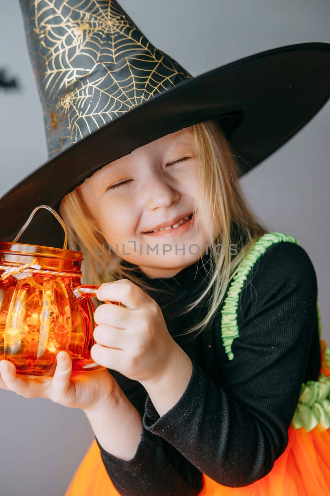 Children's Halloween - a girl in a witch hat and a carnival costume with airy orange and black balloons at home. Ready to celebrate Halloween.