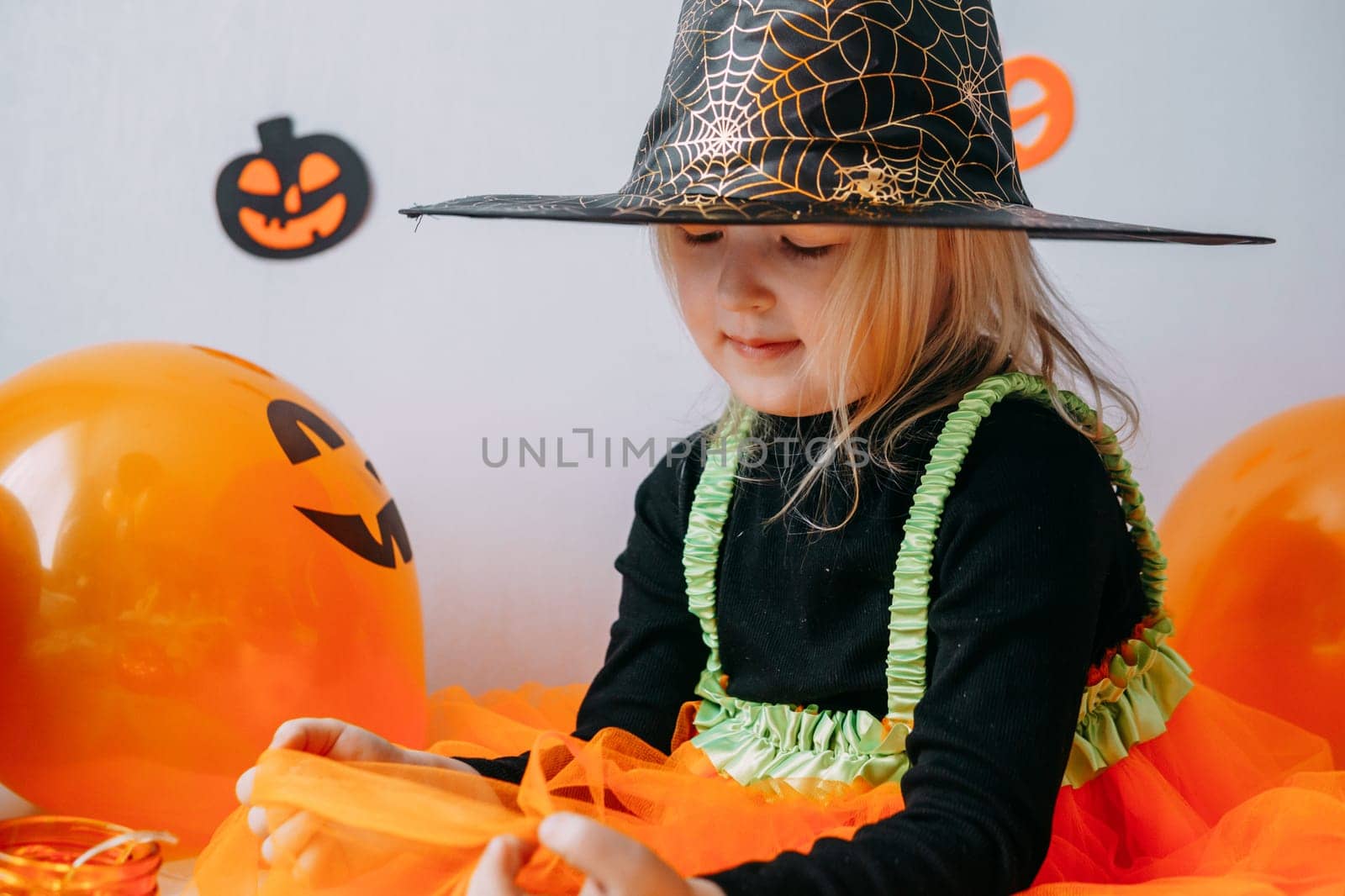 Children's Halloween - a girl in a witch hat and a carnival costume with airy orange and black balloons at home. Ready to celebrate Halloween.
