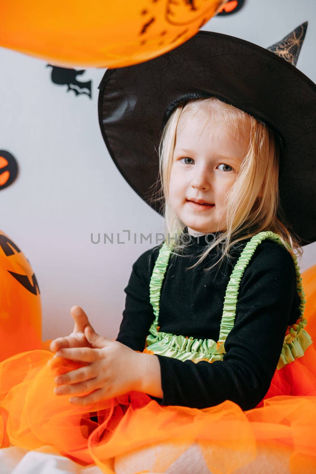 Children's Halloween - a girl in a witch hat and a carnival costume with airy orange and black balloons at home. Ready to celebrate Halloween.