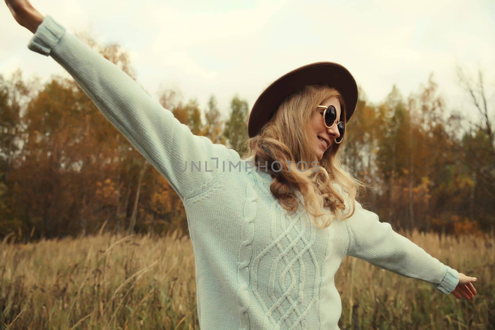 Autumn portrait of stylish modern happy young woman having fun and dancing, fashionable girl smiling in hat, sweater outdoors in park, warm fall season